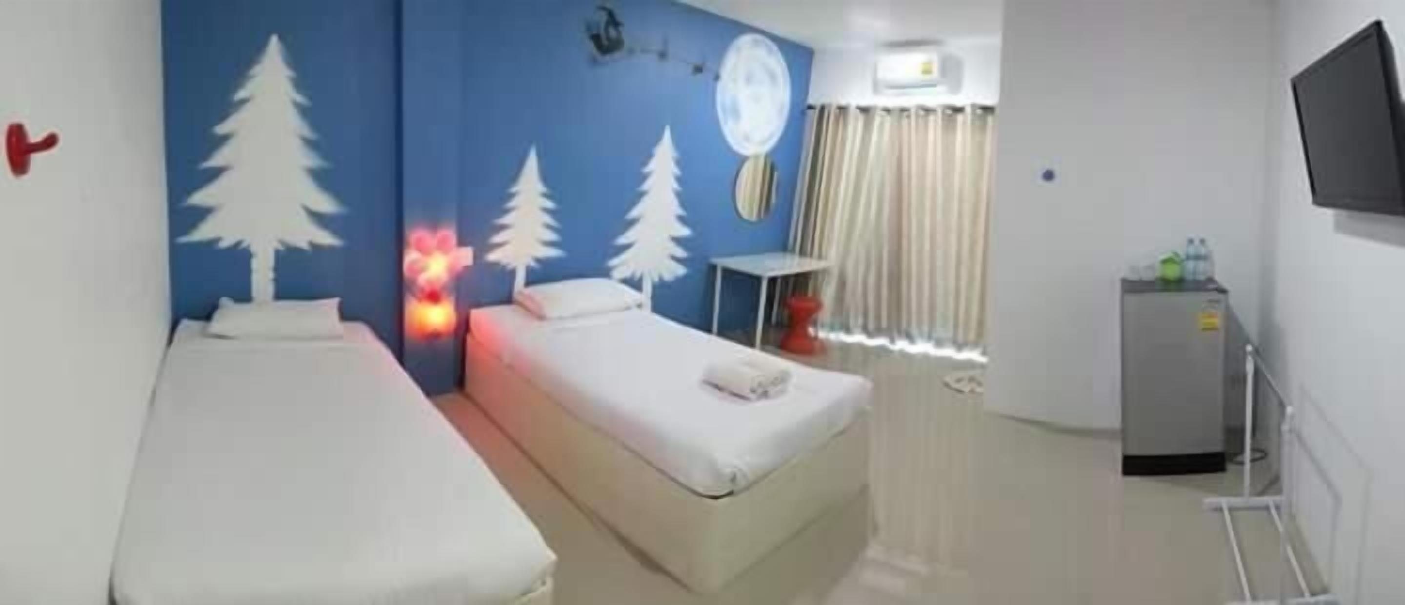 A hotel room with two beds, a small table, a TV, and a window with curtains.