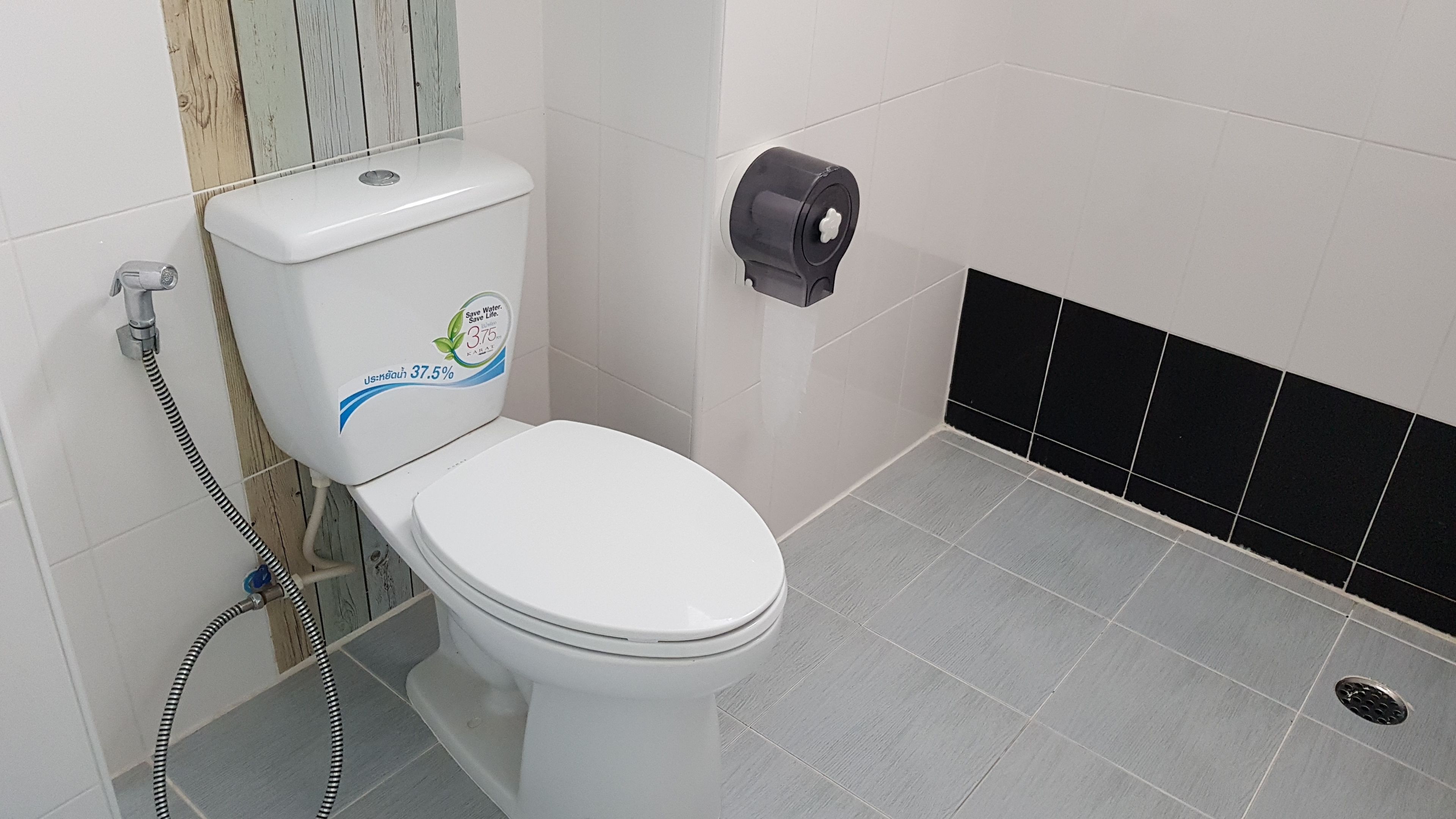 A white toilet with a water-saving sticker, a toilet paper holder, and a shower hose.