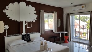 Un dormitorio con una cama grande, un escritorio, una silla, un taburete rojo, una ventana con cortinas y un aire acondicionado de pared.