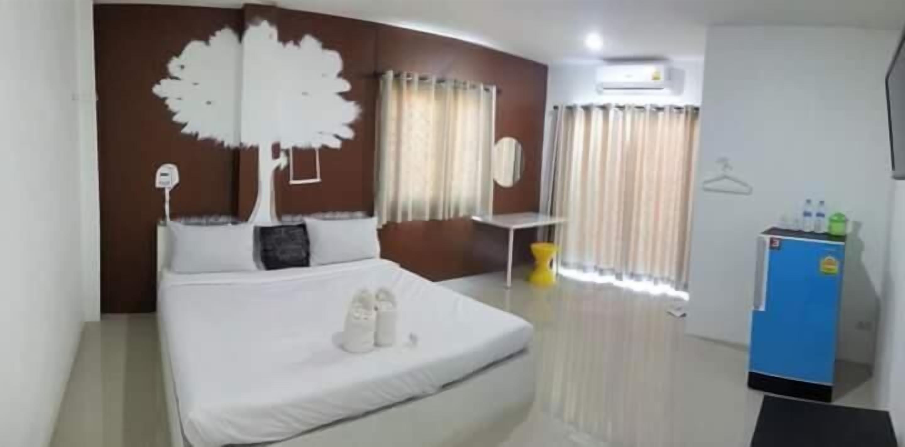 A hotel room with a bed, a dresser, a mirror, a window with curtains, and a small table.