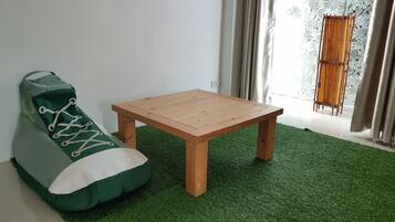 Um quarto com uma poltrona de veludo verde, uma mesa de madeira e uma janela com cortinas.