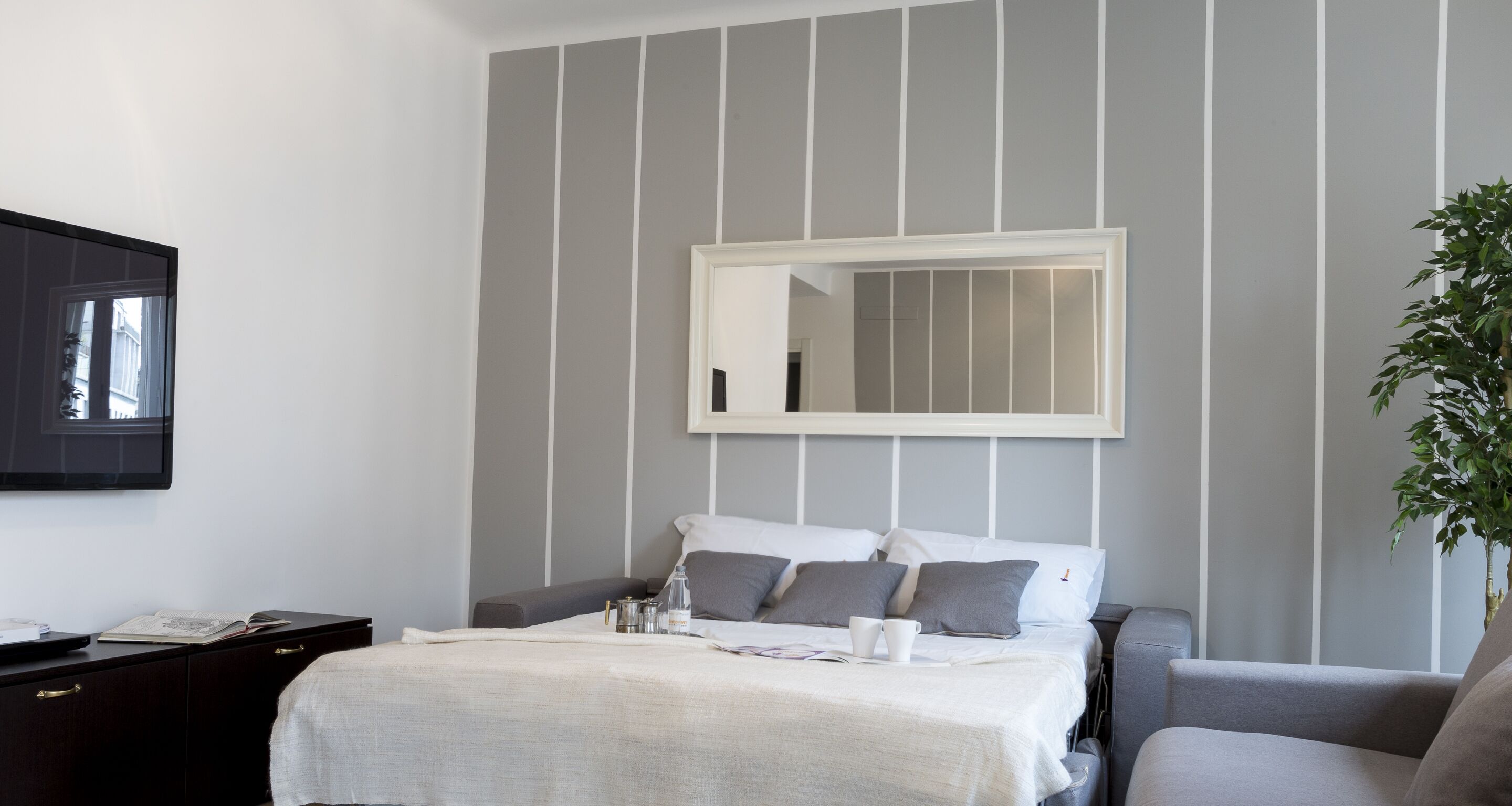 A modern hotel room with a bed, bedside table, and a large mirror.