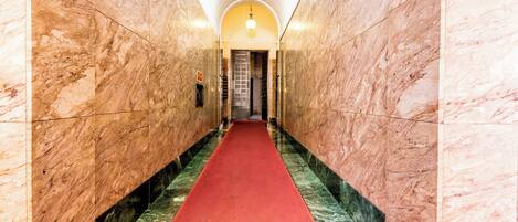 Un couloir en marbre, avec un tapis rouge menant à une porte.