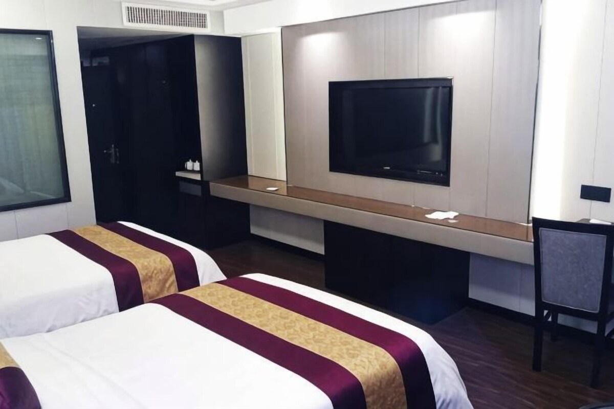 Habitación de hotel con dos camas, televisión, escritorio y armario.