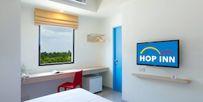 Habitación de hotel moderna con un ventanal grande, un escritorio, una silla roja, una cama y un televisor que muestra el logotipo de 'Hop Inn'.