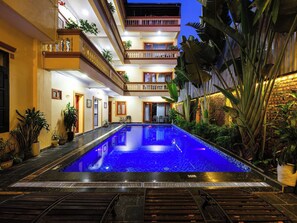 Un hôtel à plusieurs étages doté d’une piscine centrale, de balcons et d’une végétation tropicale luxuriante.