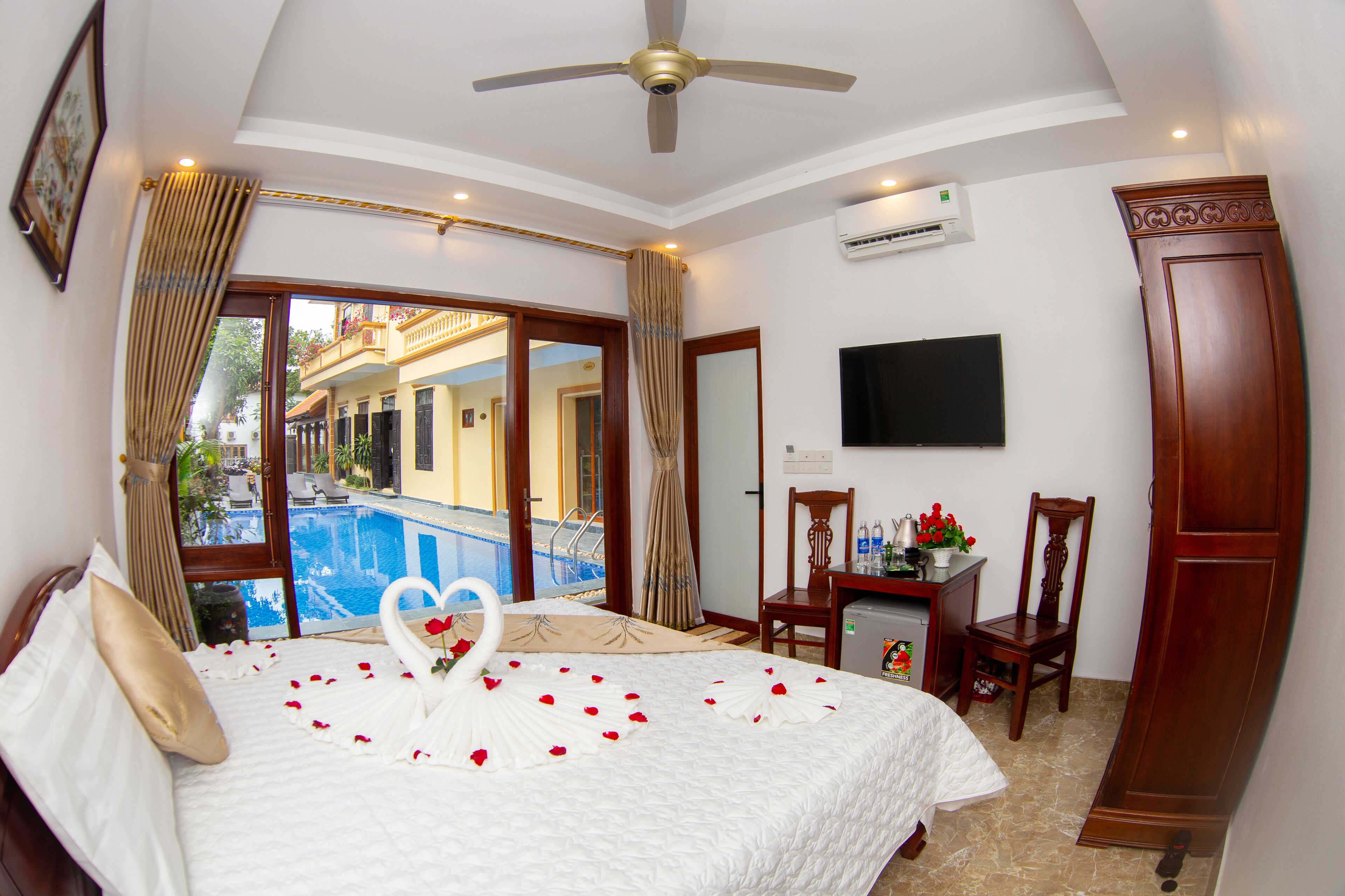 A hotel room with a bed, a desk, a TV, and a view of a pool.