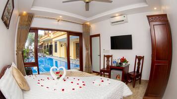 A hotel room with a bed, a desk, a TV, and a view of a pool.