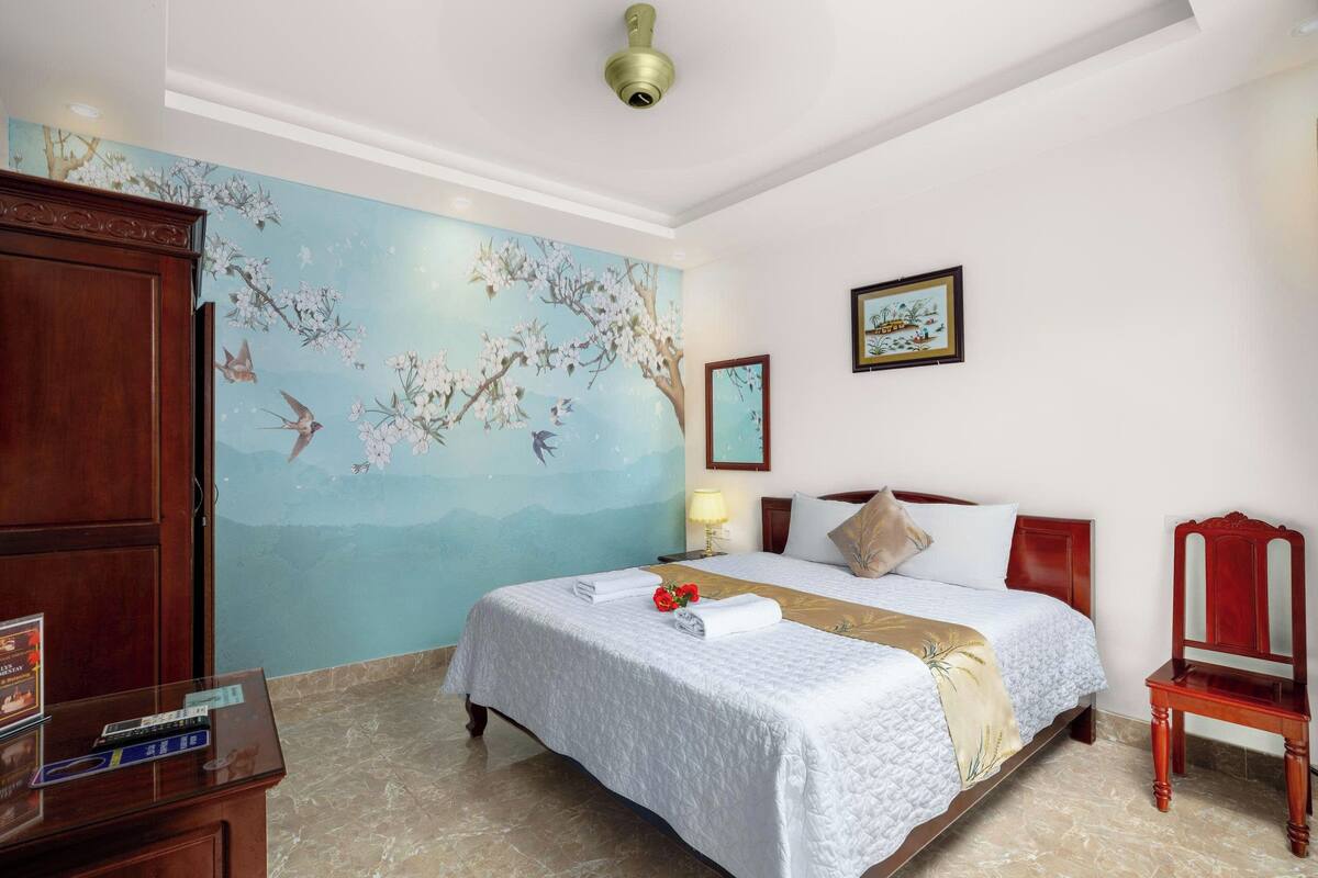 Ein Hotelzimmer mit einem Bett, einem Holzschrank, einem Schreibtisch mit Lampe und einem Bild an der Wand.