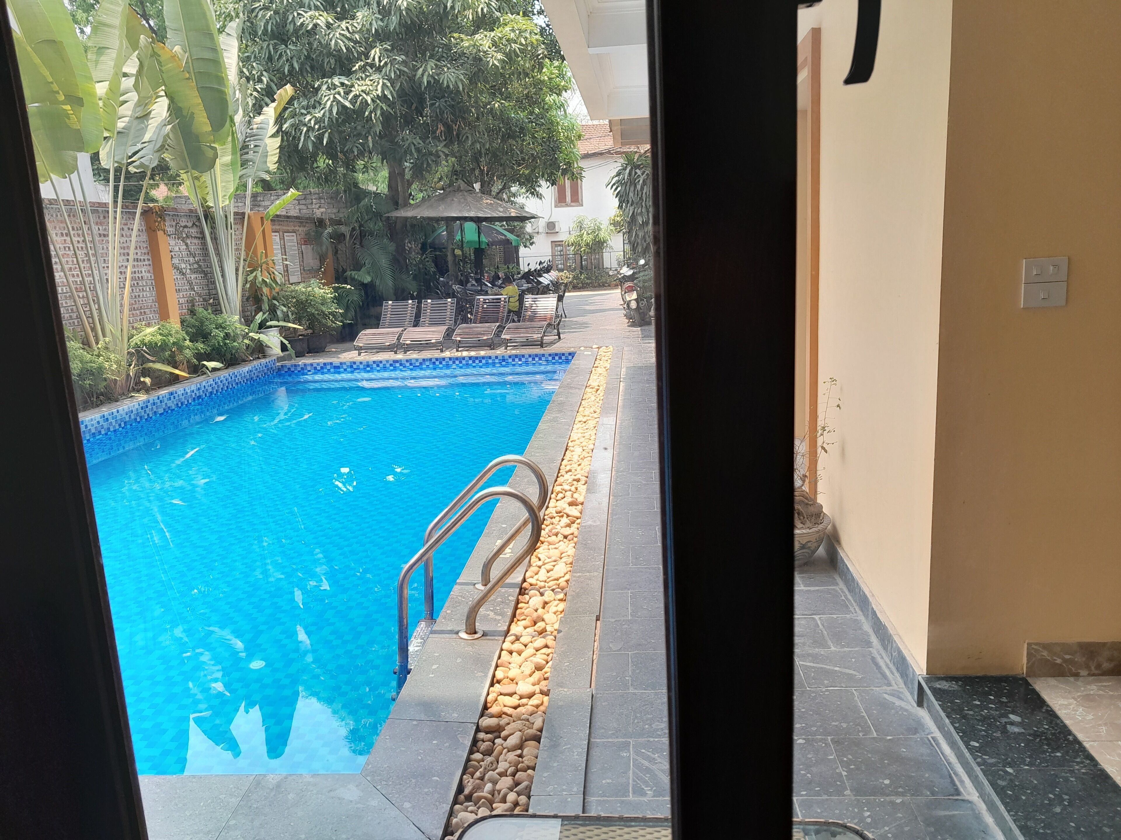 Una piscina con borde de azulejos, cantos de piedra y una escalera de metal.