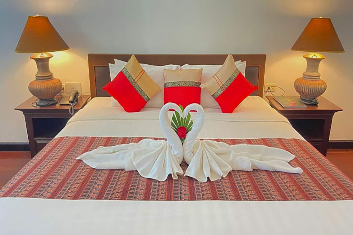 Ein Hotelzimmer mit einem ordentlich bezogenem Bett, zwei Nachttischlampen und einer dekorativen Schwanen-Handtuch-Arrangement auf der Bettdecke.