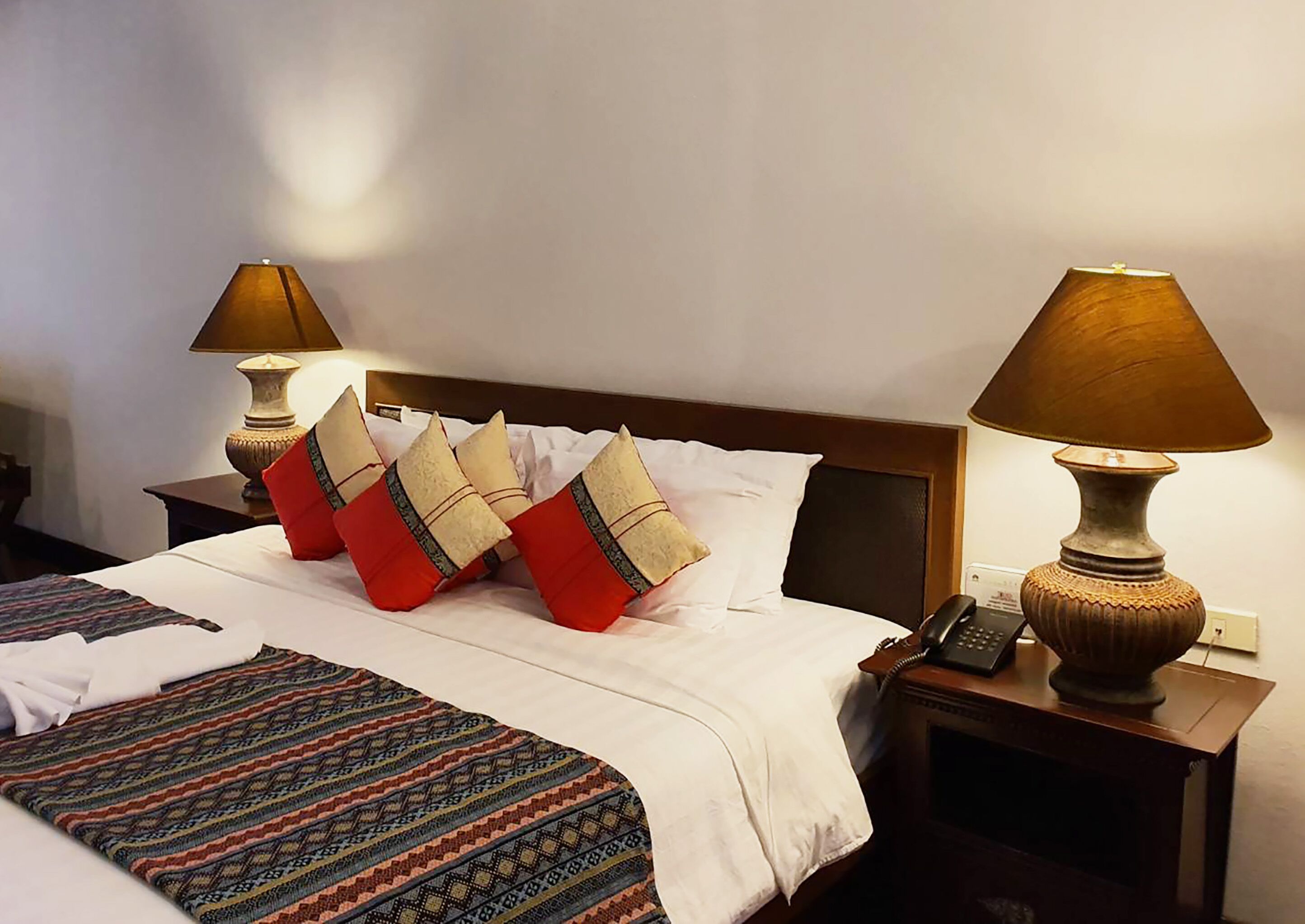 A hotel room with a neatly made bed, two bedside lamps, a telephone, and a patterned throw blanket.