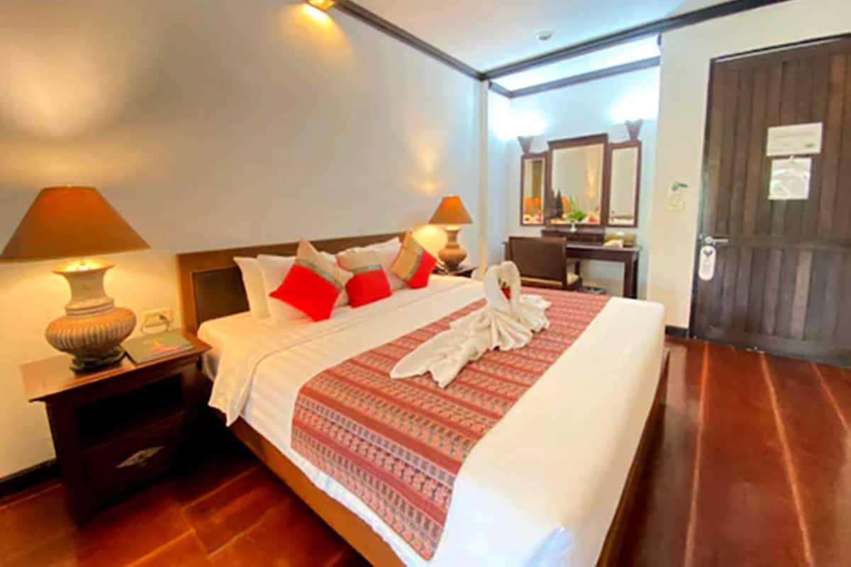 Ein Hotelzimmer mit einem ordentlich bezogenen Bett, zwei Nachttischlampen, einem Holznachttisch, einem Holzboden, einem Schreibtisch mit Stuhl und einer Tür mit einem Schild.