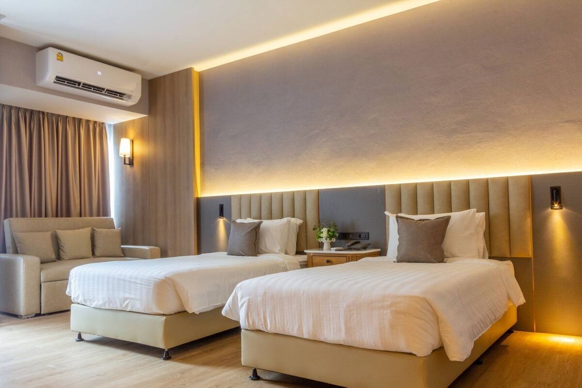 Ein modernes Hotelzimmer mit zwei Betten, einer Couch, einem Nachttisch und einer Klimaanlage.
