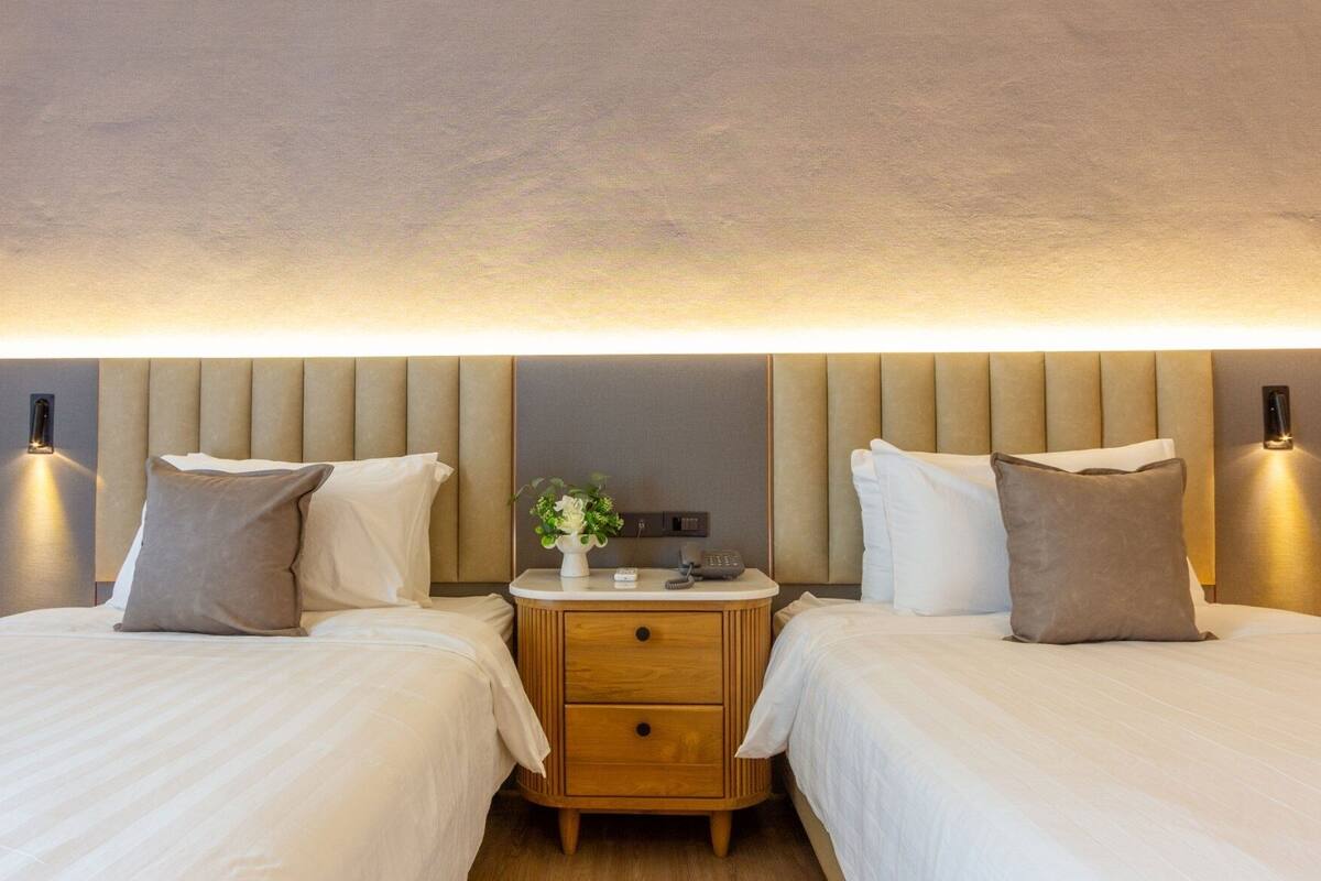 Ein Hotelzimmer mit zwei Betten, einem Nachttisch mit Blumenvase und Wandleuchten.