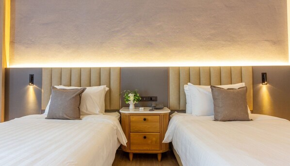 A hotel room with two beds, a bedside table with a vase of flowers, and wall-mounted lights. - Gassan Khuntan Golf and Resort (Mae Tha)