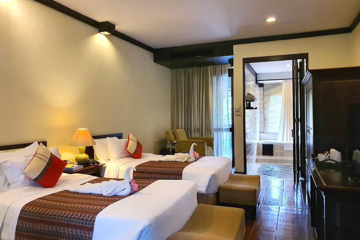 Ein Hotelzimmer mit zwei Betten, einem Schreibtisch, einem Stuhl und einem durchgehenden Türrahmen einsehbarer Badezimmer.