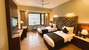 A hotel room with two beds, a desk, a chair, a TV, and a window with curtains. - The Kargil (Kargil)