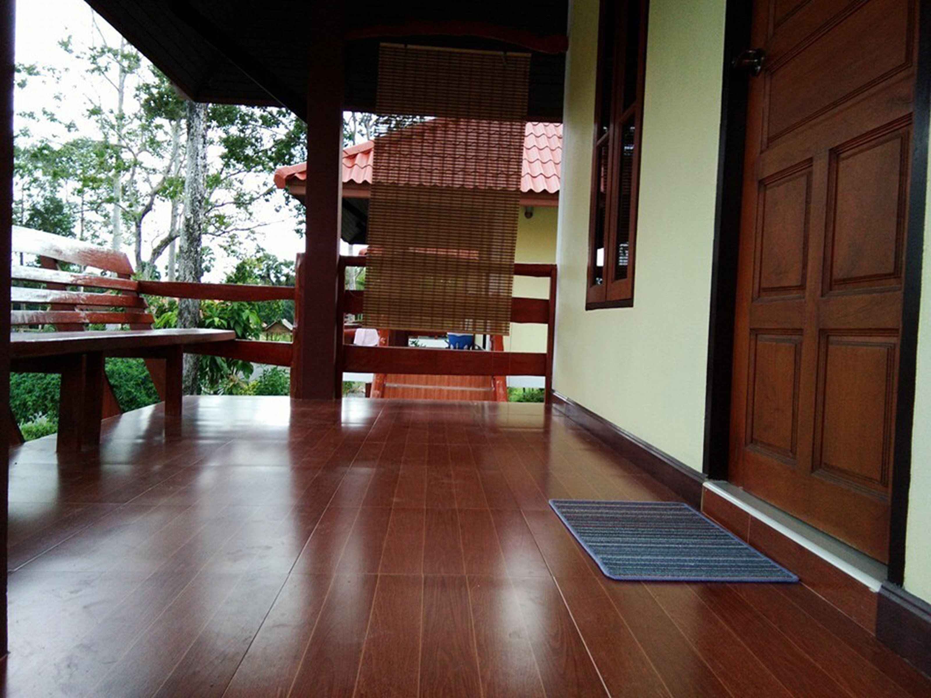 A wooden porch with a bench, a door, and a view of greenery outside.