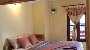 Une chambre à coucher avec un lit, des oreillers, une table de chevet, un miroir et une fenêtre avec des rideaux.