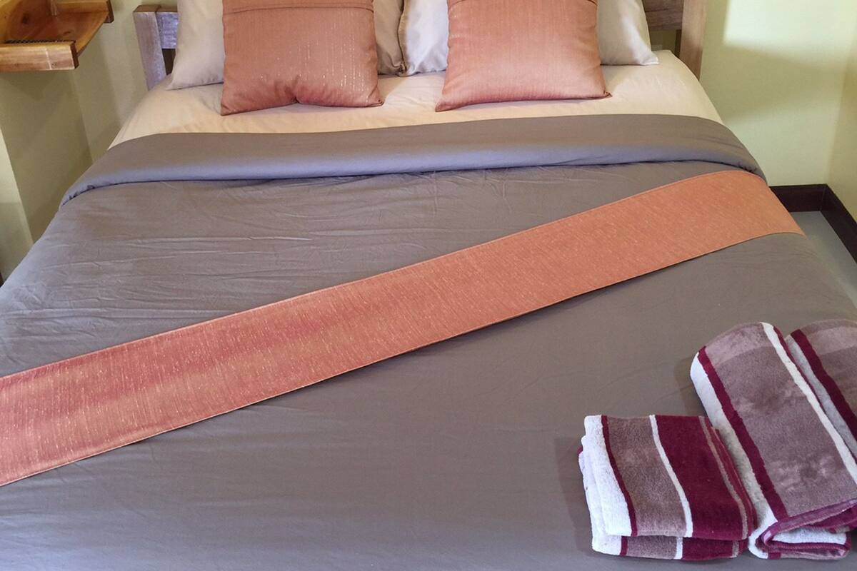 Ein Bett mit einer grauen und orangefarbenen Bettdecke, zwei Kissen und zwei gefaltete Handtücher.