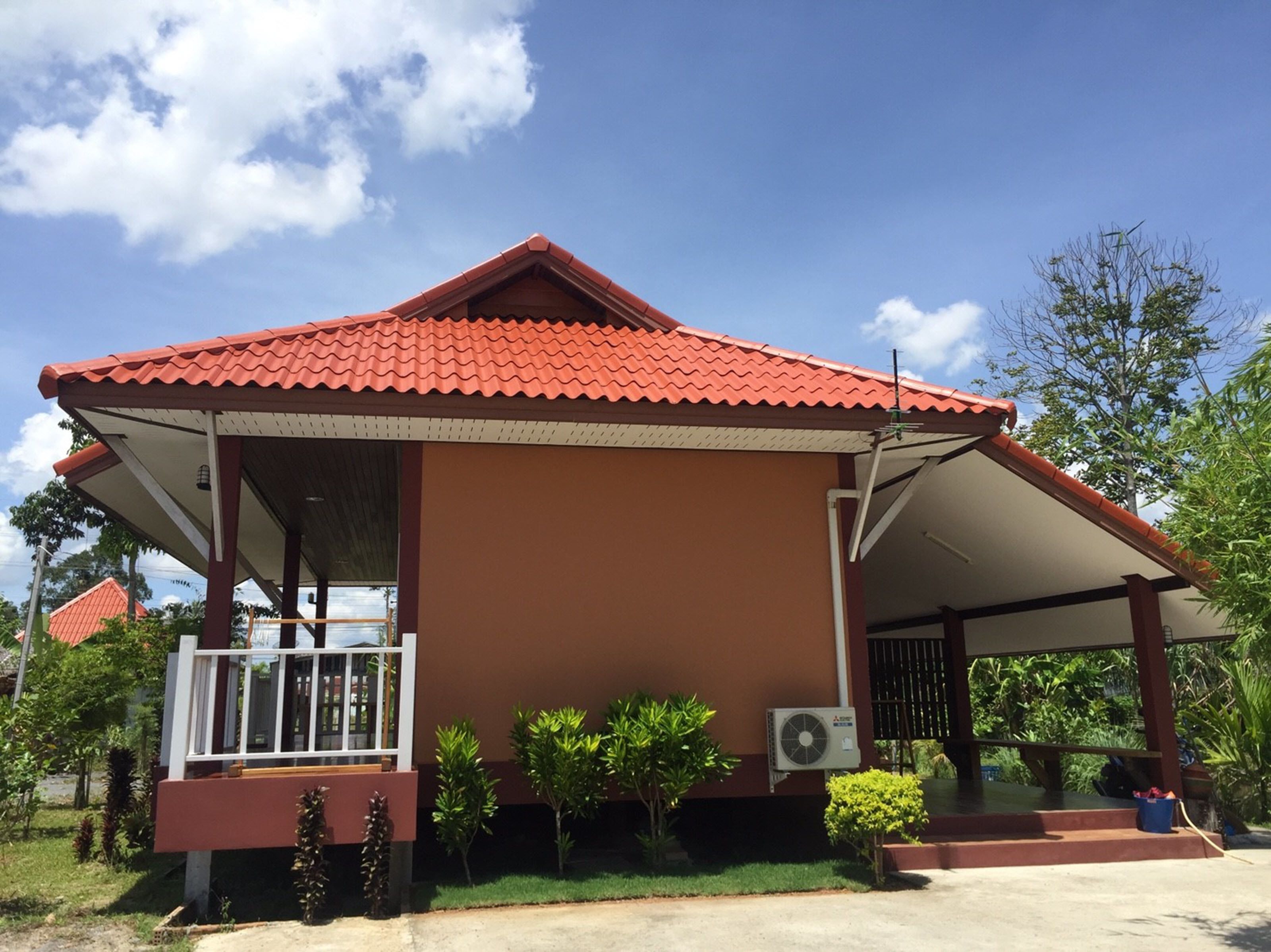 A building with a red-tiled roof, a covered porch, and a small garden area with various plants.
