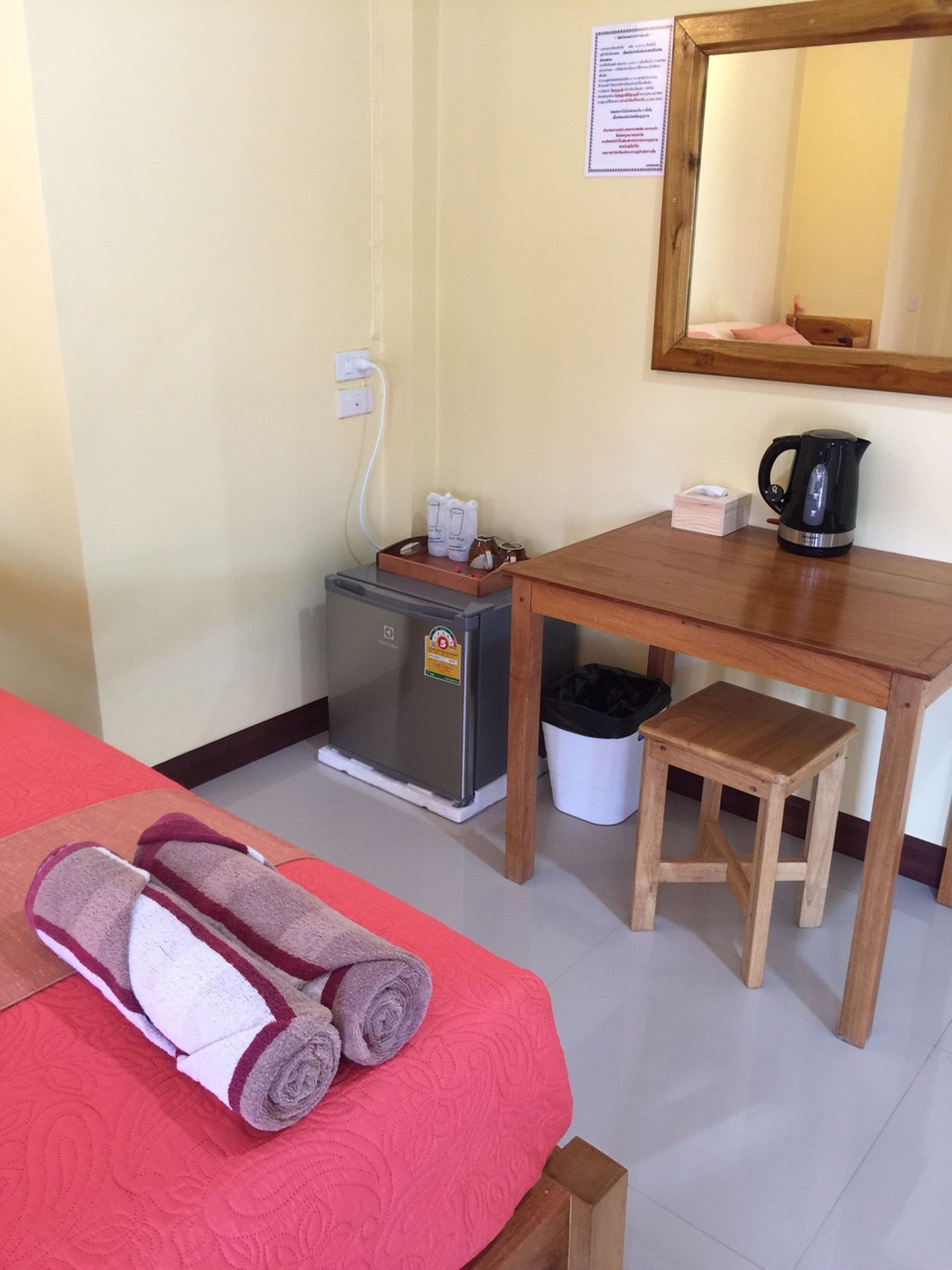 Una habitación de hotel con una cama, una kitchenette pequeña, una mesa de madera, un taburete y un espejo en la pared.