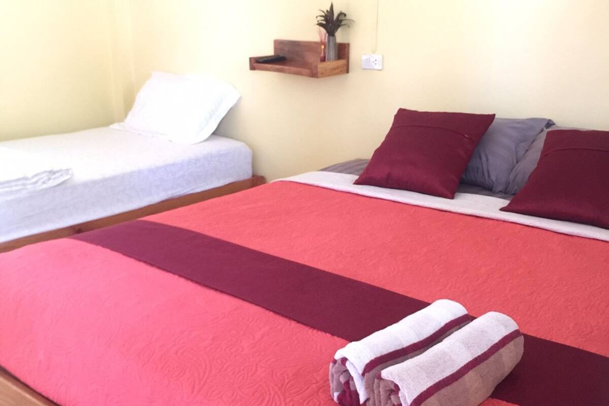 Ein Doppelbett mit rotem und weißem Bettbezug, ein Holz-Kopfteil und eine kleine Ablage mit einer Pflanze.