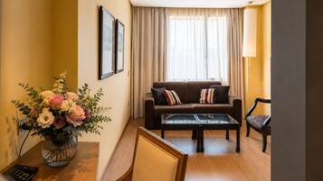 Un salón con sofá, mesa de centro, un jarrón de flores, una lámpara y un sillón.