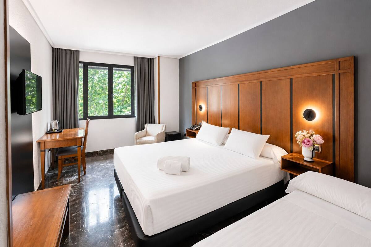 Habitación de hotel con una cama grande, un escritorio, una silla, un televisor y una ventana con cortinas.