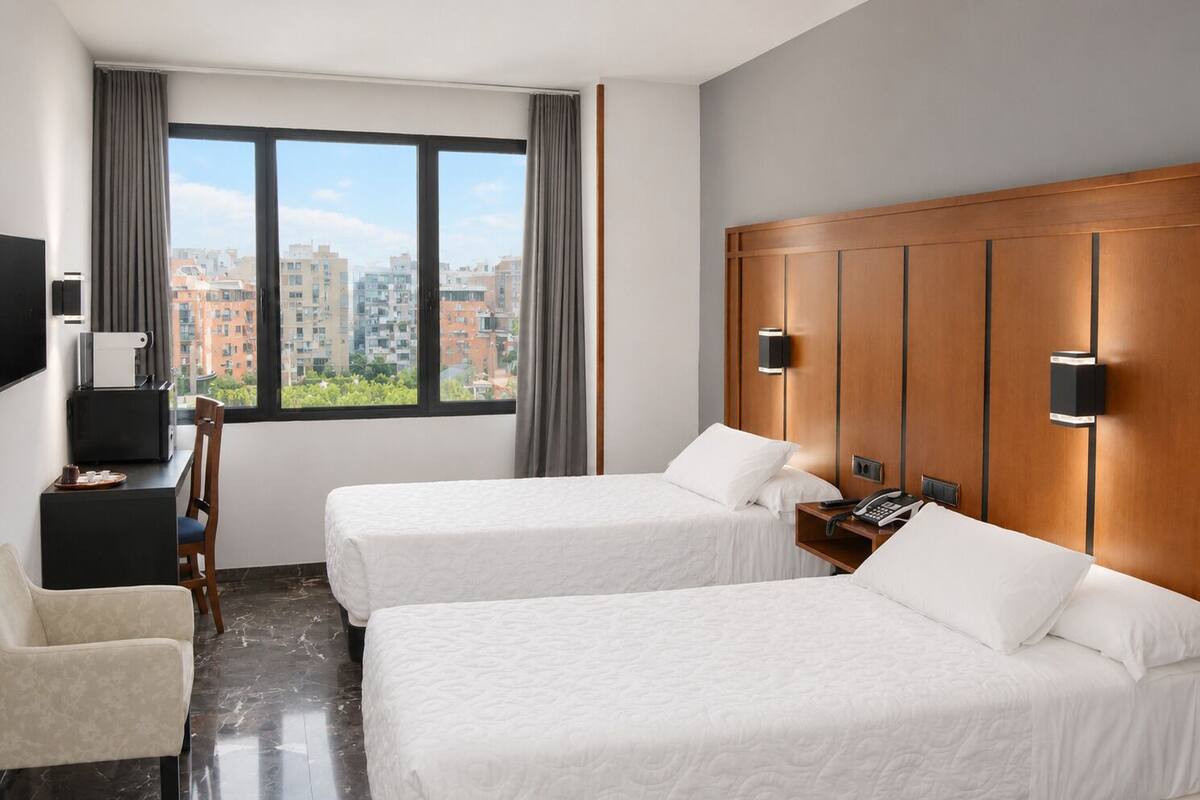 Habitación de hotel con dos camas, un escritorio, una silla, un televisor y vista a la ciudad.