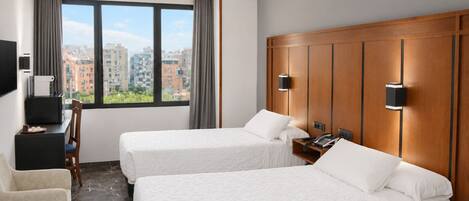 Habitación de hotel con dos camas, un escritorio, una silla, un televisor y vista a la ciudad.