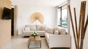A modern living room with a sofa set, a coffee table, a wall-mounted fan, and a large window with a view.