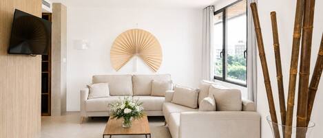 Un salon moderne comprenant un ensemble de canapés, une table basse, un ventilateur fixé au mur et une grande fenêtre donnant sur un beau paysage.