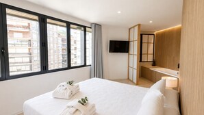 A hotel room with a large bed, a TV, a wooden partition, and a view of the city.