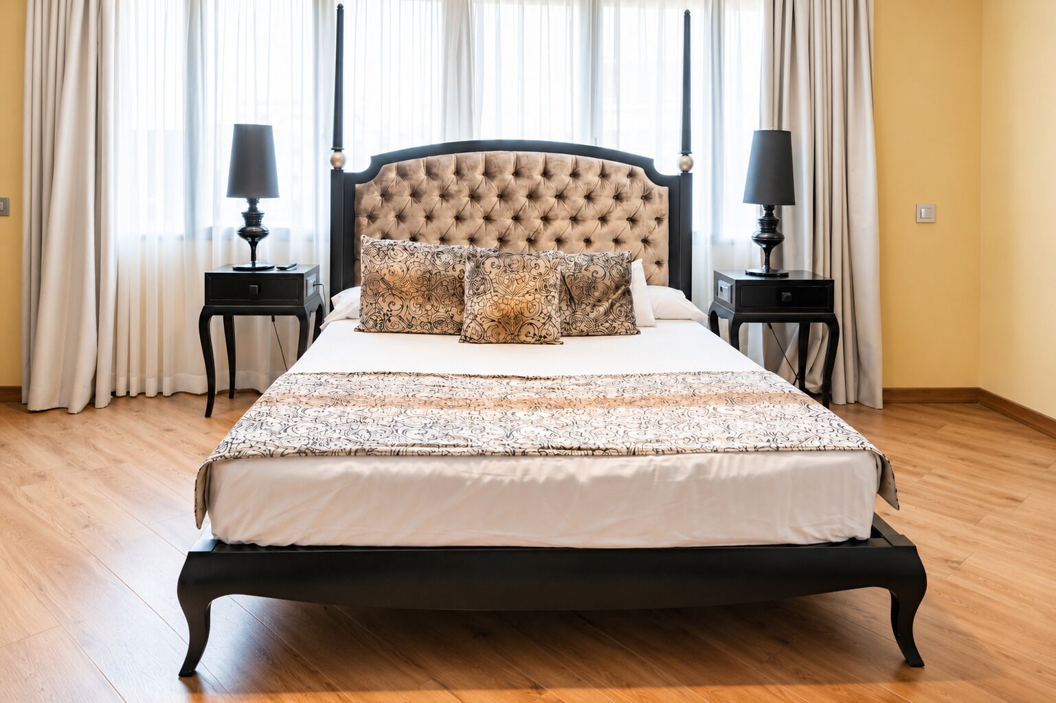 A large bed with a tufted headboard, two bedside tables, and patterned bedding.