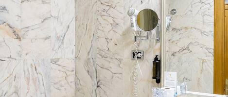 A bathroom with a marble wall, a toilet, a sink with a mirror, and a hairdryer.