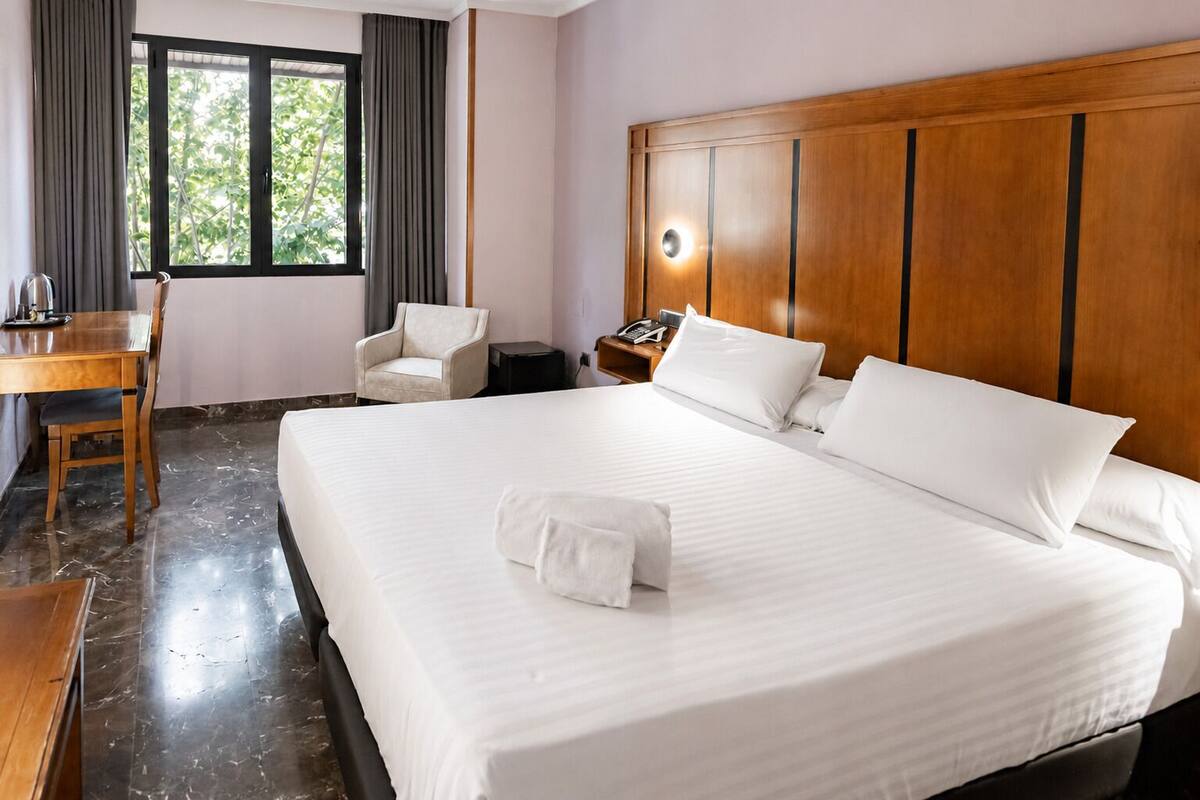 Una habitación de hotel con una cama grande, un escritorio, una silla y una mesita de noche con un teléfono.