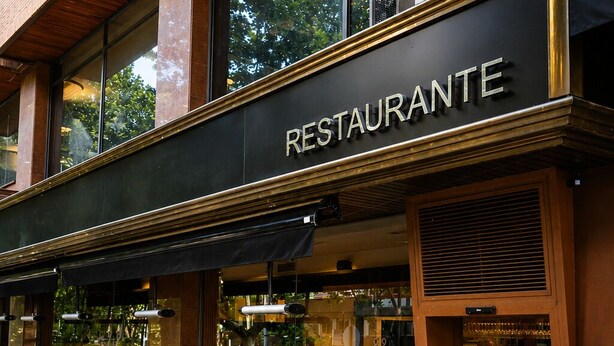 A restaurant with a black awning, outdoor seating, and large windows.