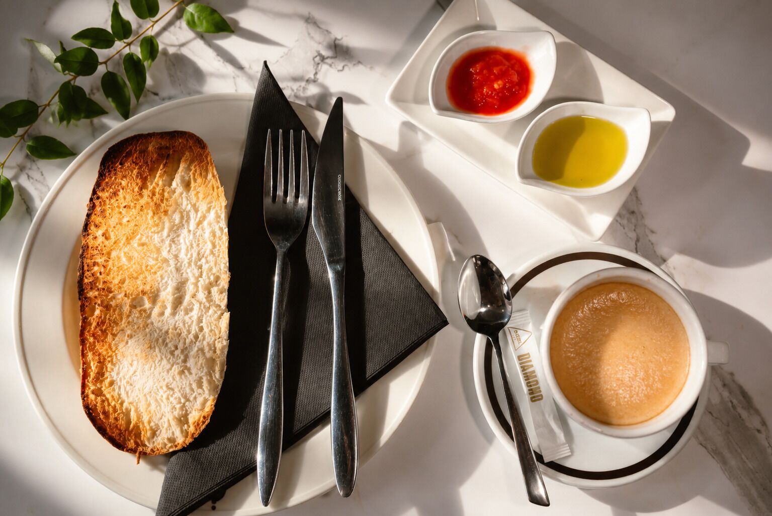 A breakfast setting with toast, cutlery, a cup of coffee, and two small bowls of condiments.