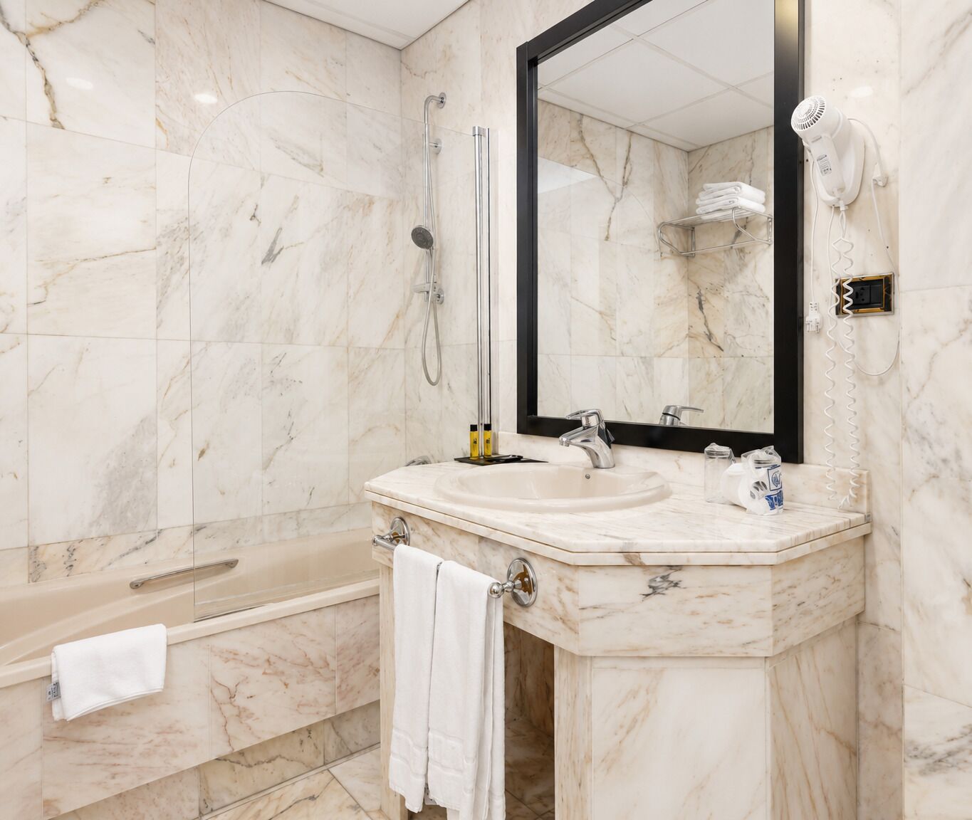 A modern bathroom with a marble sink, a large mirror, a handheld showerhead, and a towel rack.
