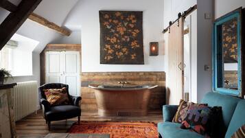 Una habitación con una bañera grande, un sillón de cuero negro, un sofá azul y una alfombra estampada.