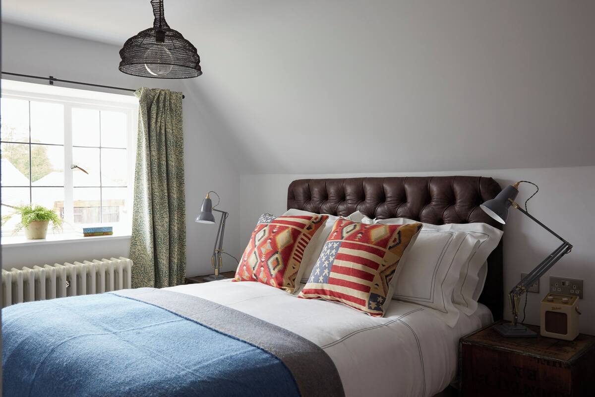A bedroom with a large bed, a window with curtains, a radiator, and a bedside table with a lamp.