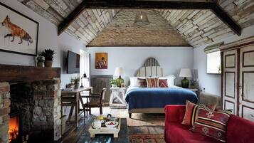 A rustic bedroom with a fireplace, a bed with a blue bedspread, a red sofa, and a wooden table with a tray of breakfast.
