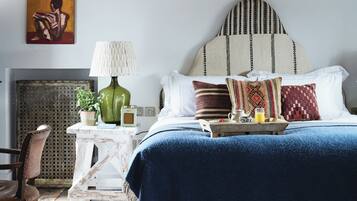 A bedroom with a bed, pillows, a bedside table with a lamp, a chair, and a painting on the wall.