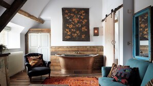 Une pièce comprenant un fauteuil en cuir noir, un canapé turquoise, une grande baignoire et un tapis aux couleurs vives.