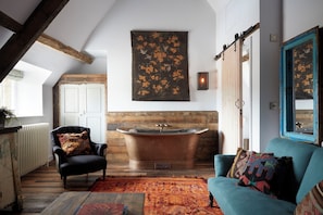 A room with a black leather armchair, a teal sofa, a large bathtub, and a colorful rug.