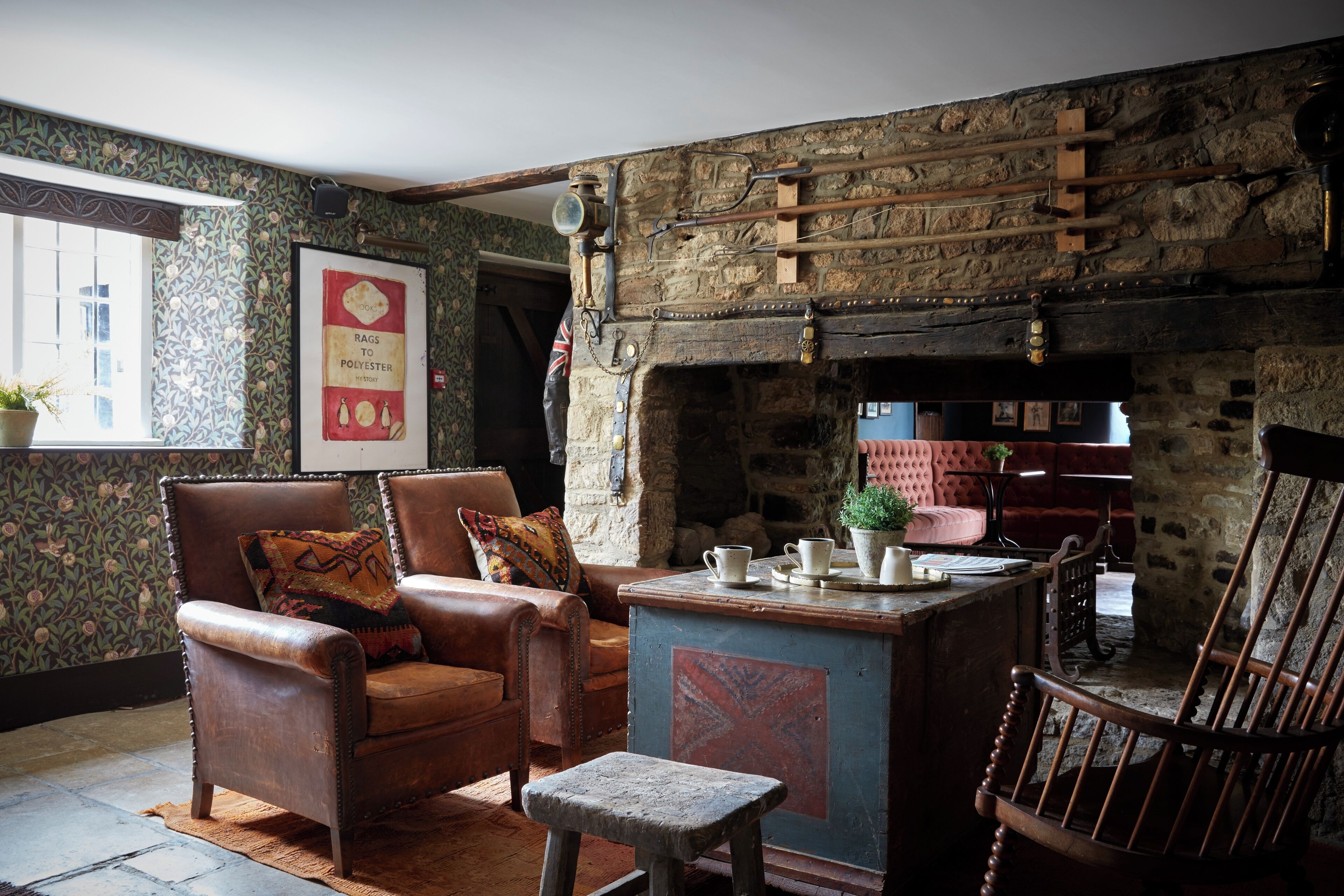 A rustic room with a stone fireplace, leather armchairs, and a small table with cups and saucers.