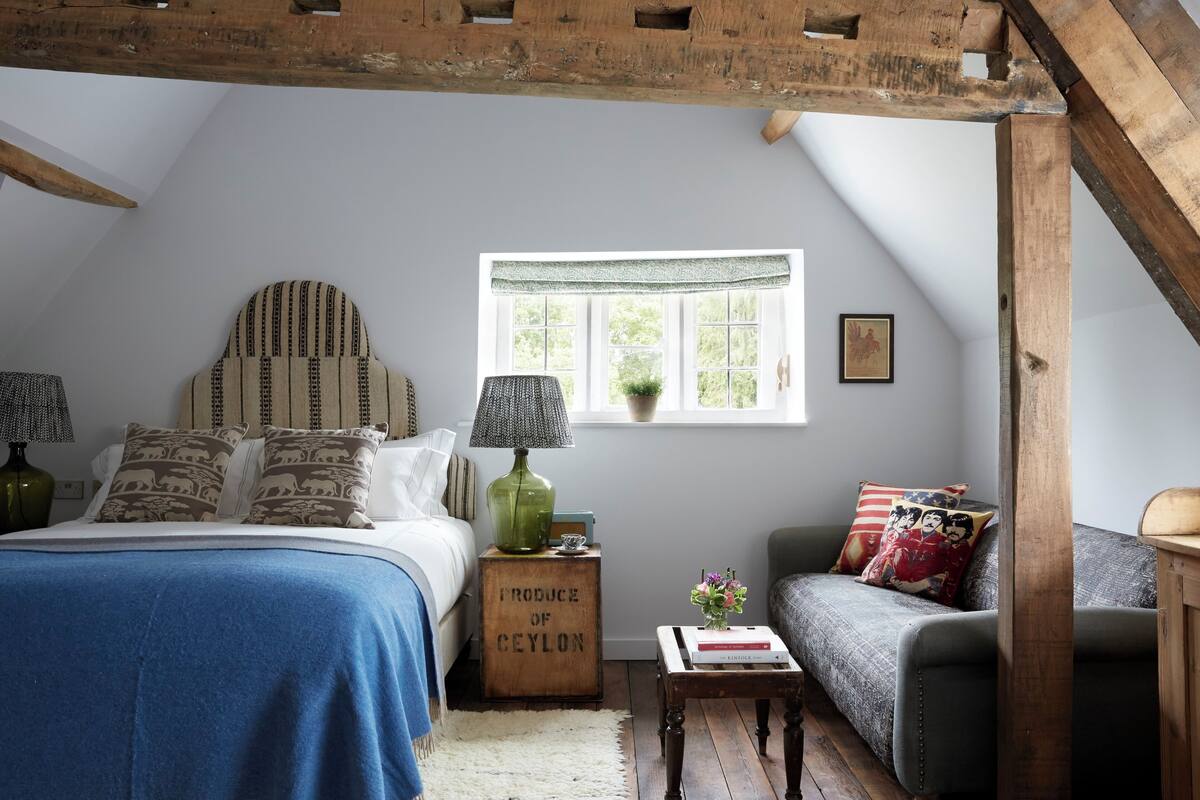 A cozy bedroom with a bed, a sofa, a window with a view, and a wooden crate labeled "PRODUCE OF CEYLON".