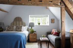 A cozy bedroom with a bed, a sofa, a window with a view, and a wooden crate labeled "PRODUCE OF CEYLON".